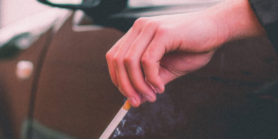 Hand håller i cigarett ut genom fönstret på en bil.